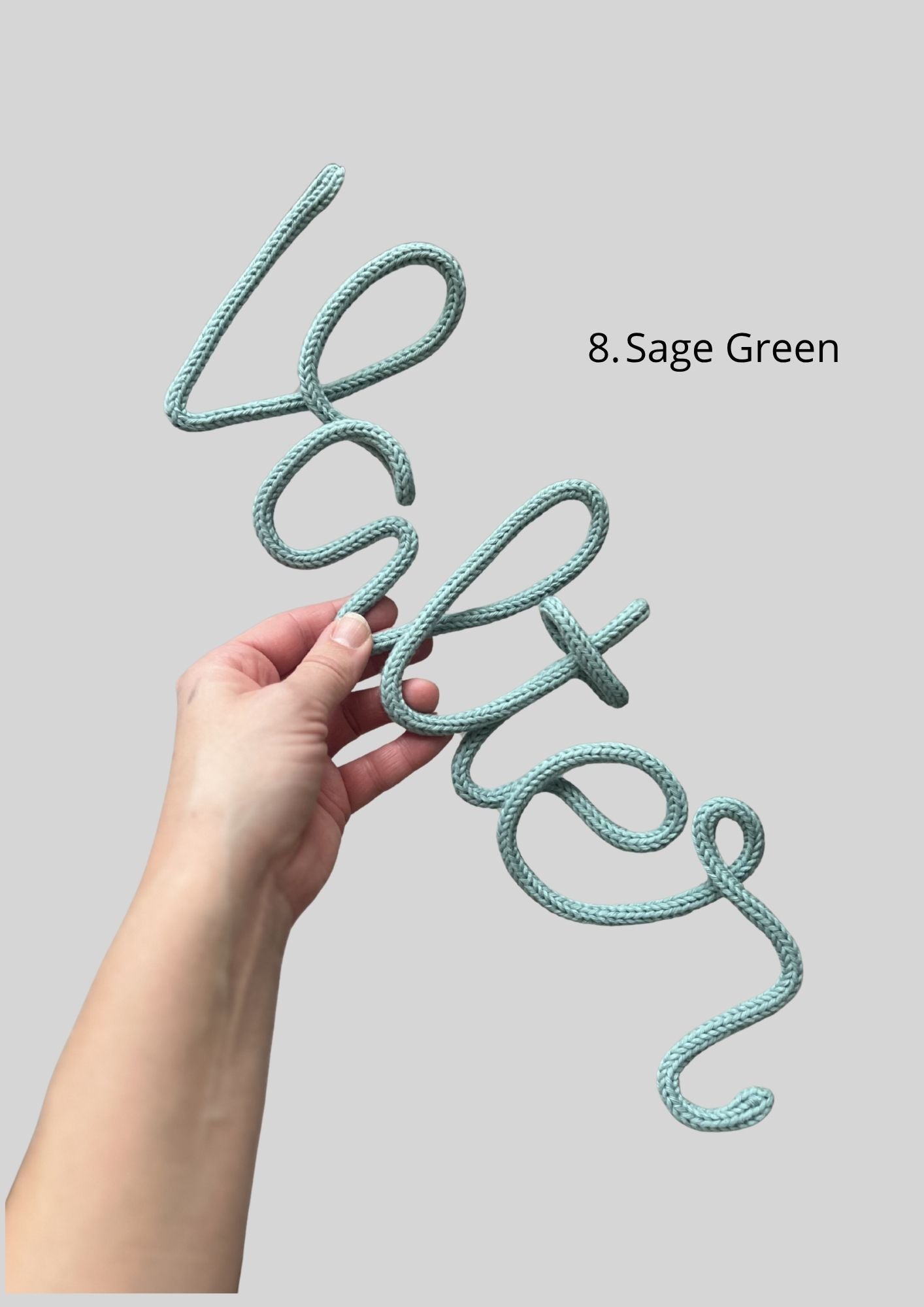 Hand holding a knitted name in color sage green. The name is valter