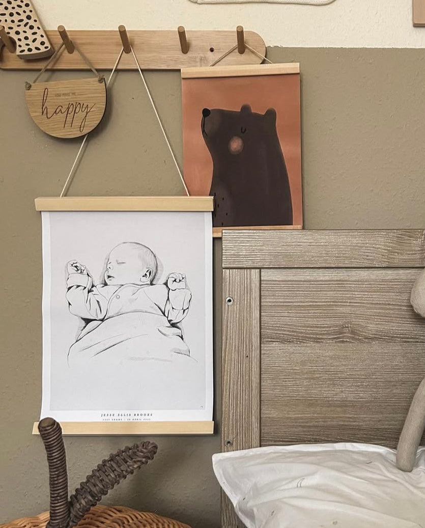 Hand-drawn personalized birth poster displayed in a wooden poster hanger in a child's room.
